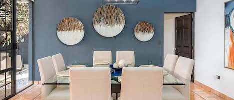Un comedor con mesa de vidrio, sillas blancas y decoración en la pared.