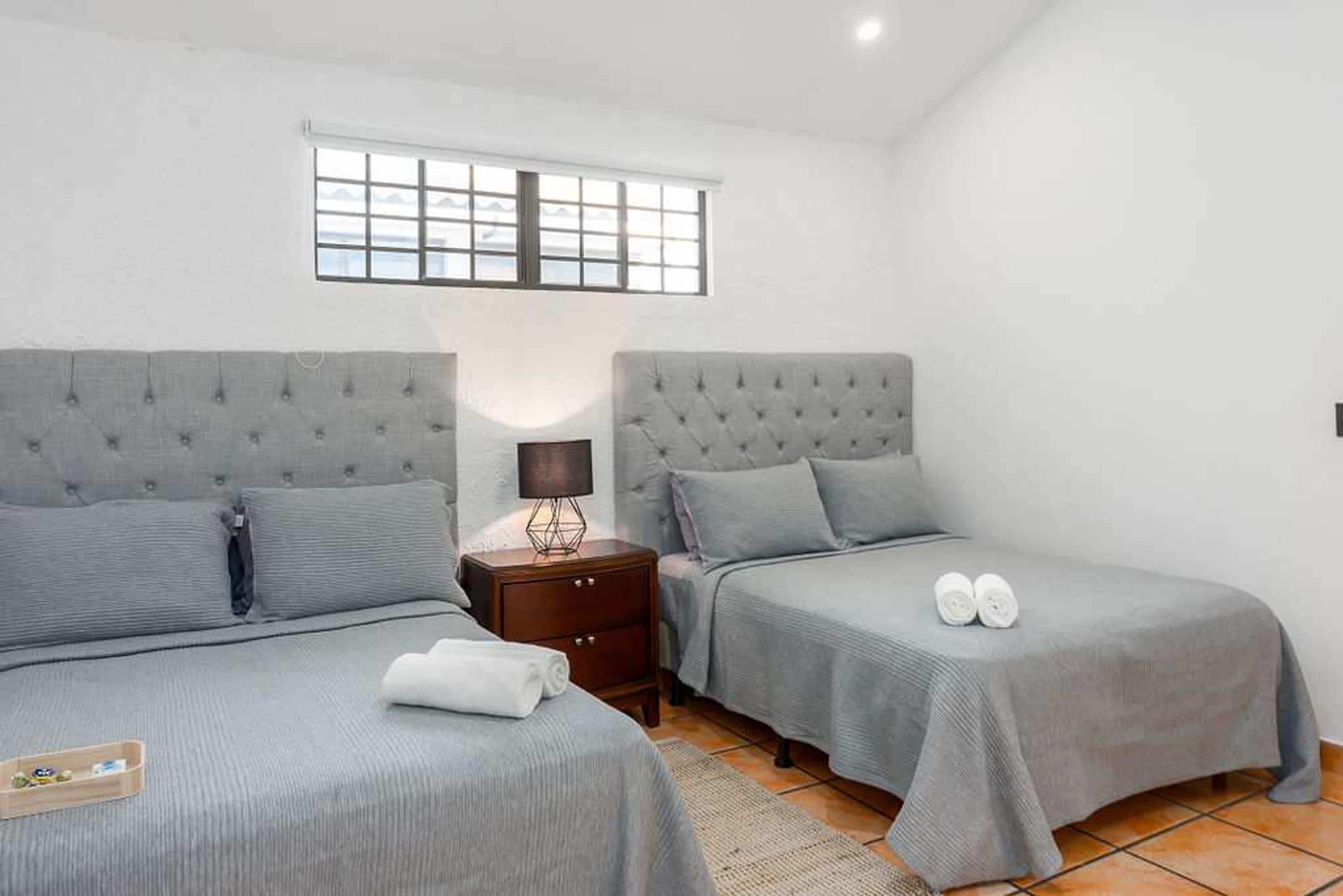 A twin bedroom with two beds, a nightstand, a lamp, and a window.