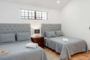 A twin bedroom with two beds, a nightstand, a lamp, and a window.