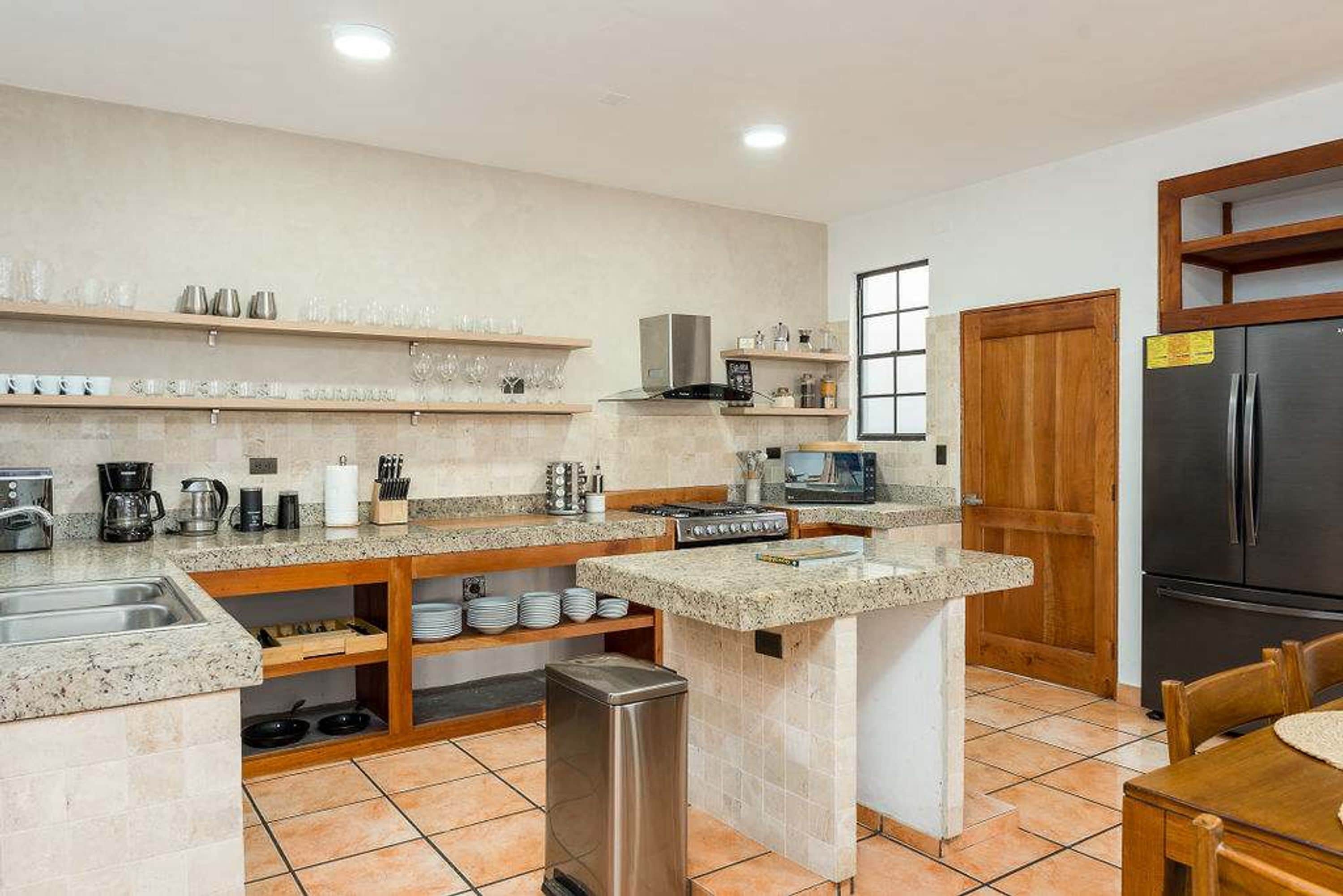 A compact kitchen with a built-in stove, a refrigerator, and a microwave. There are shelves above the counter holding various kitchen items.
