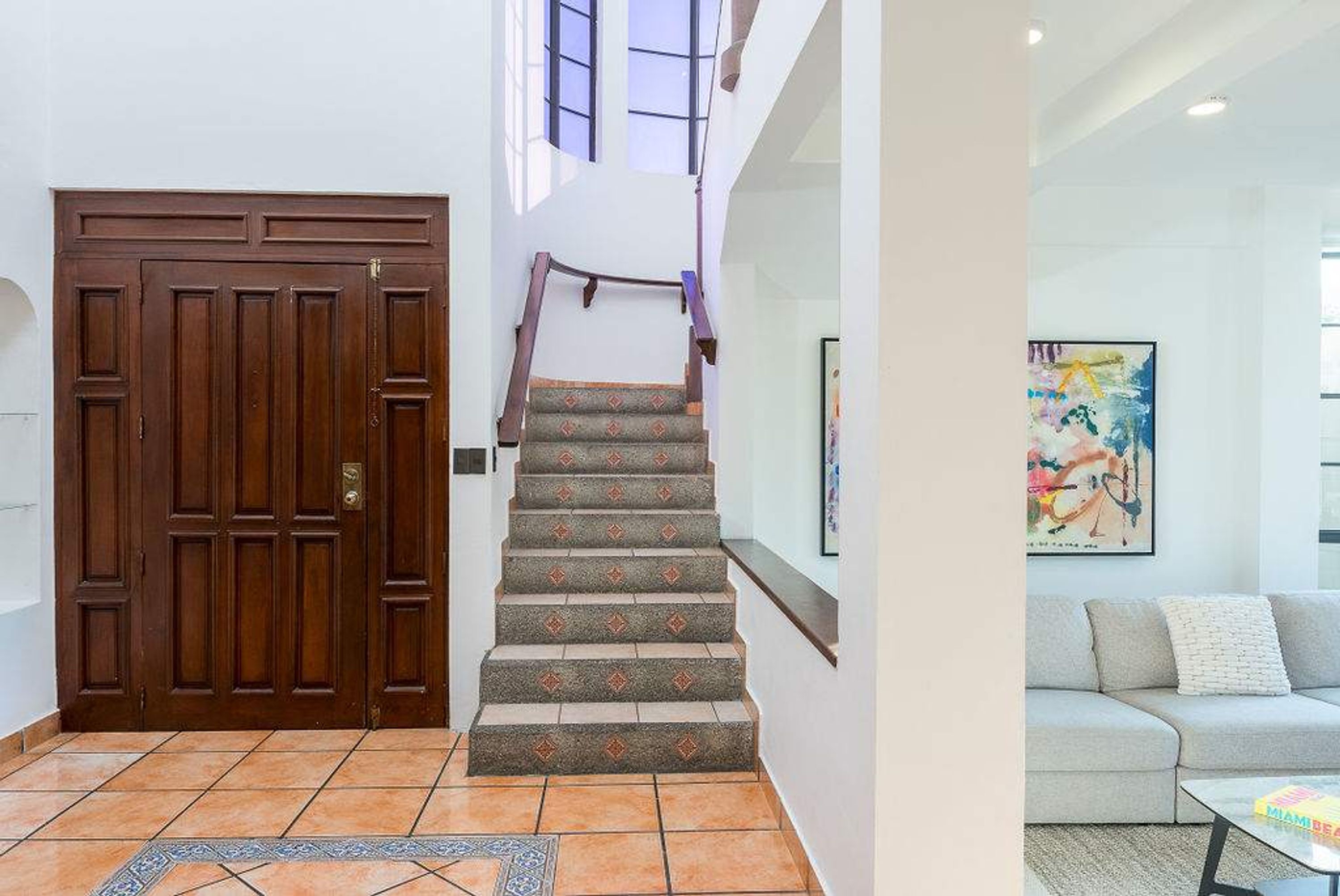 A staircase with patterned carpet leading to a landing, a wooden door, and a living area with a couch and a painting.