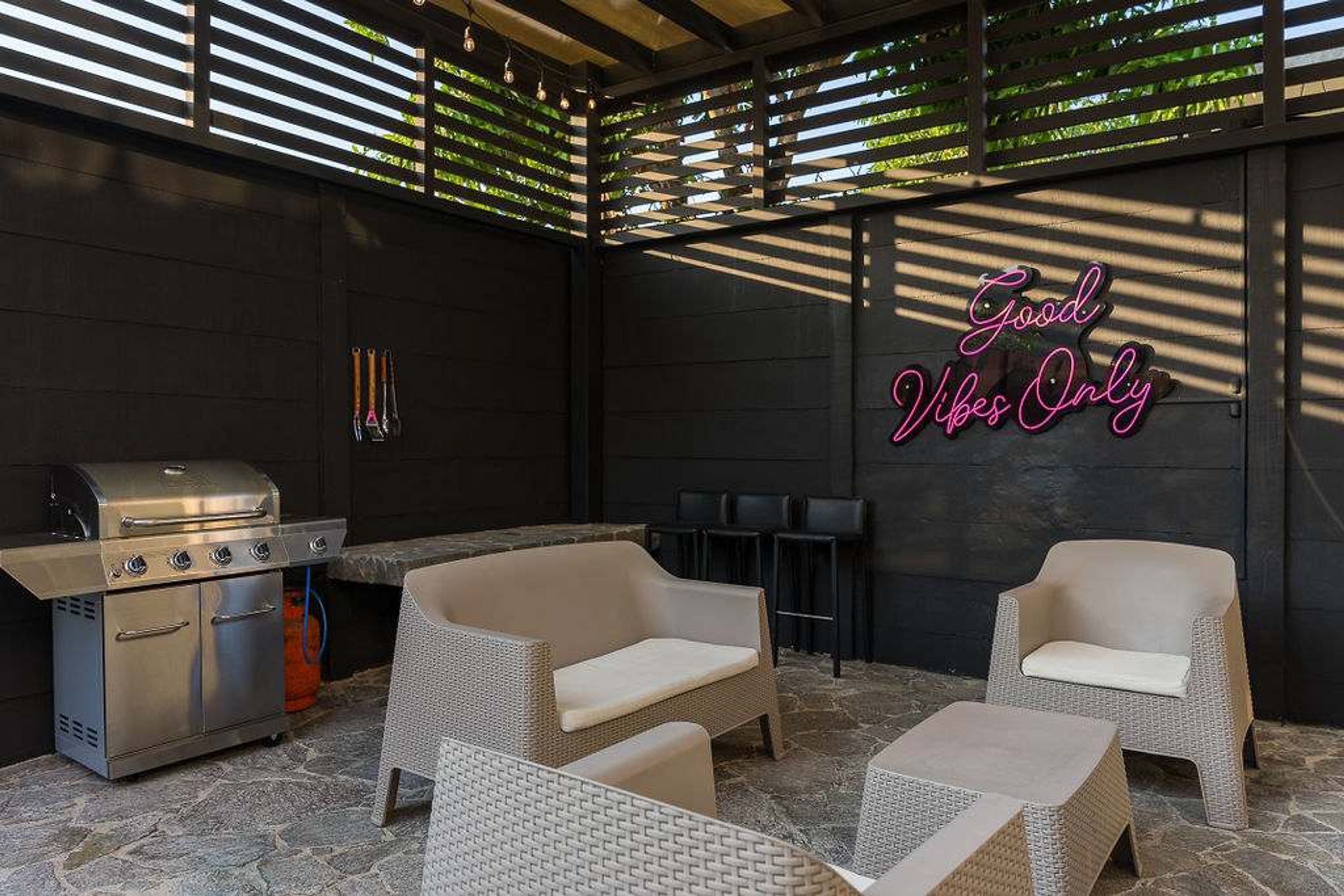 An outdoor patio with a grill, wicker furniture, and a neon sign.
