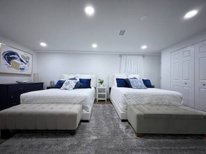 Quarto com duas camas, mesa de cabeceira, cômoda e tapete cinza.