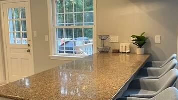 A kitchen with a granite countertop, white cabinetry, and a window with a view of greenery.