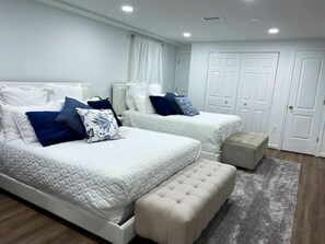 Quarto com duas camas, um banco e um guarda-roupa.