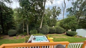 A deck with a hot tub, chairs, and a view of a well-maintained garden. - Lux Family Xcape With Hottub Fireplace Deck BBQ (Silver Spring)