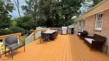 A wooden deck with outdoor furniture, a grill, and a brick building.