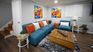 A modern living room with a blue sofa, a coffee table, and abstract paintings on the walls. - Lux Family Xcape With Hottub Fireplace Deck BBQ (Silver Spring)