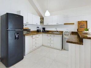 Eine kompakte Küche mit weißen Schränken, einem schwarzen Kühlschrank, einer Arbeitsplatte aus Granit und einem eingebauten Geschirrspüler.