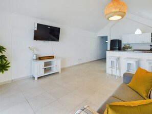 Ein modernes Wohnzimmer mit einem Flachbildfernseher, einer weißen Unterhaltungseinheit und einem Sofa mit gelbem Kissen.