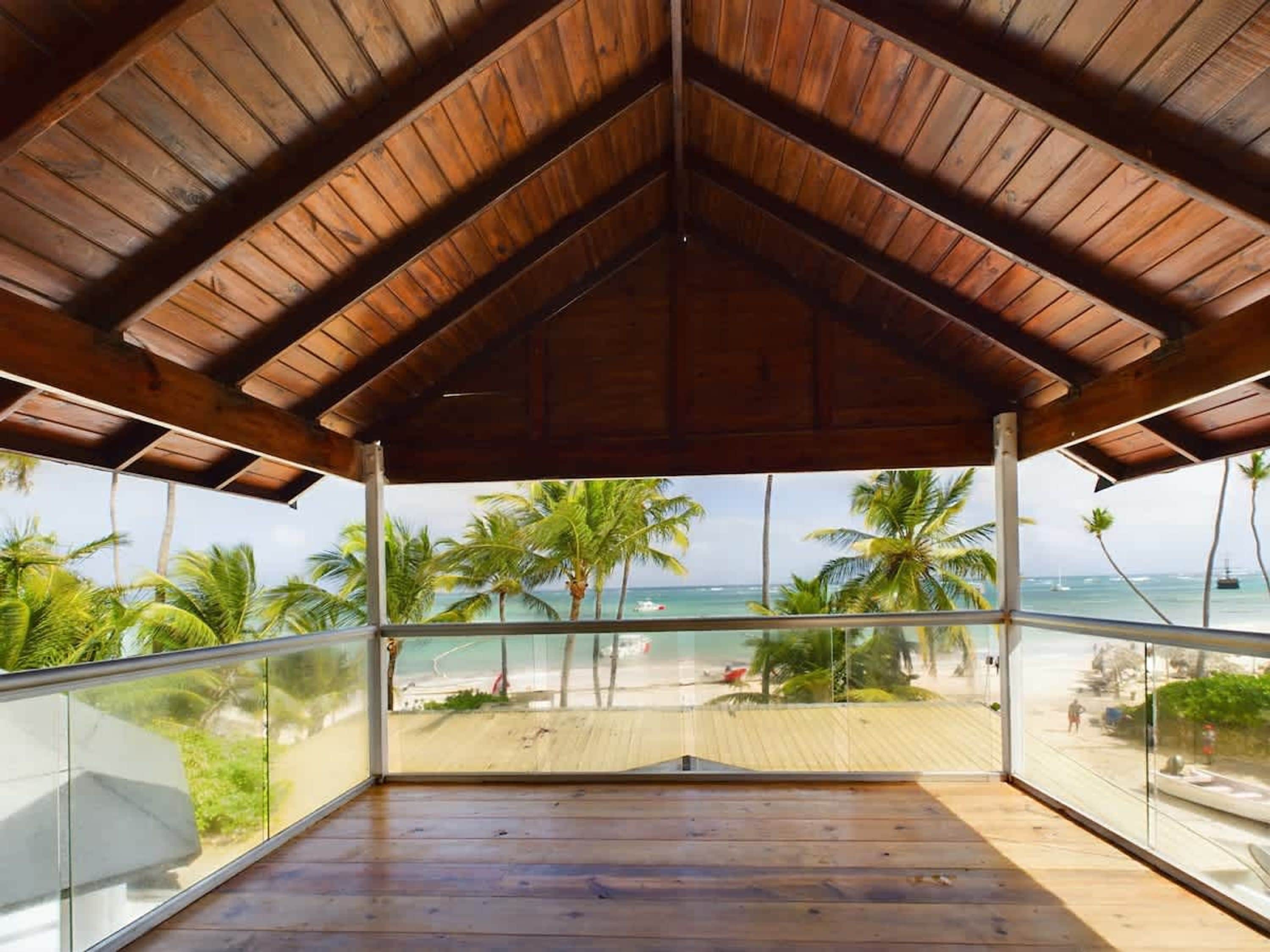 Un balcón techado con vista a una playa y palmeras.