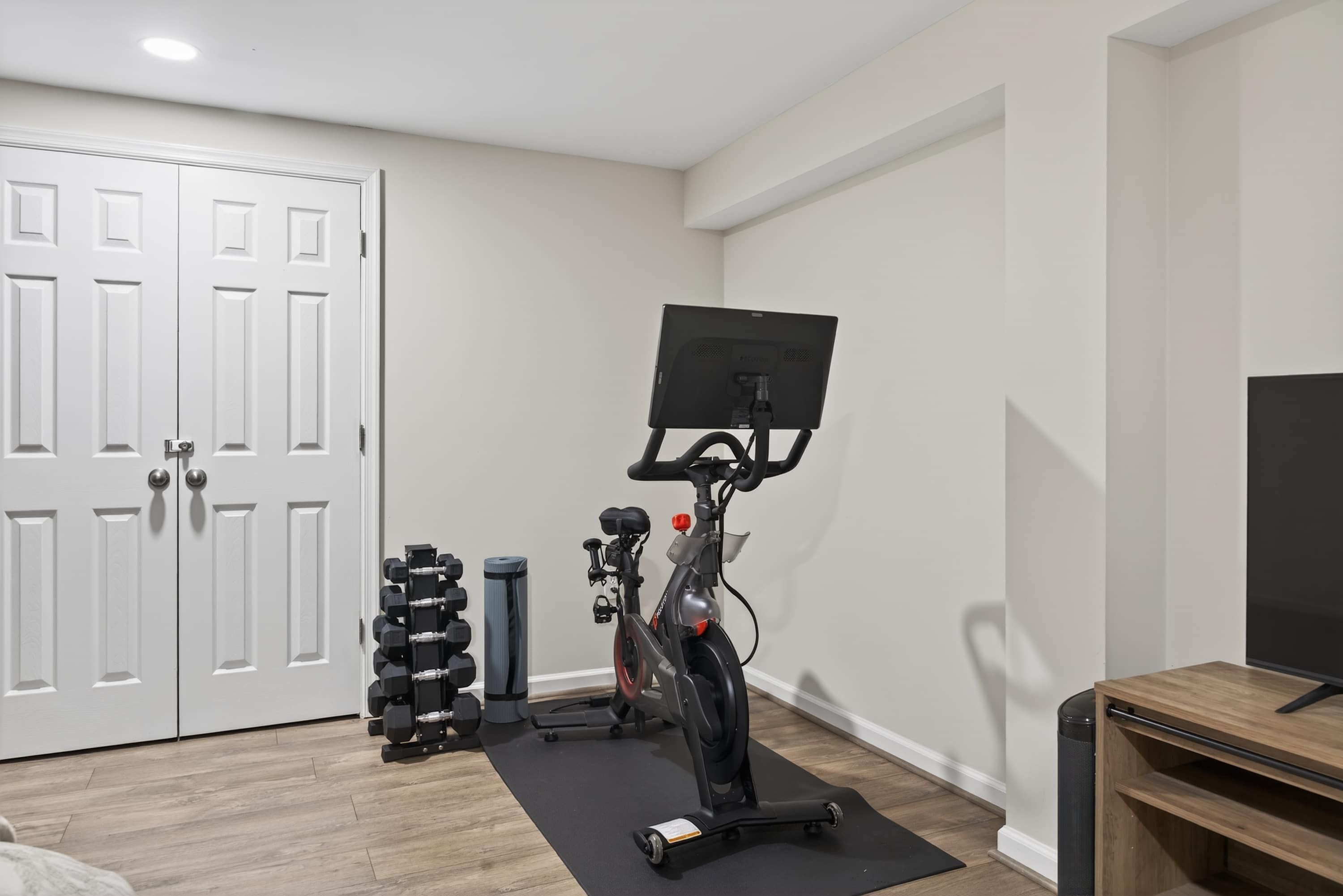 A home gym with a stationary bike, dumbbells, and a yoga mat.