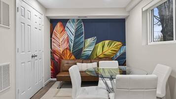 A modern room with a brown leather sofa, white chairs, a glass table, and a vibrant leaf-patterned wall.