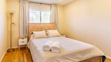 A bedroom with a bed, a nightstand, a lamp, and a window with curtains.