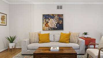 A living room with a sofa, two yellow cushions, a coffee table, a red side table, and a potted plant.