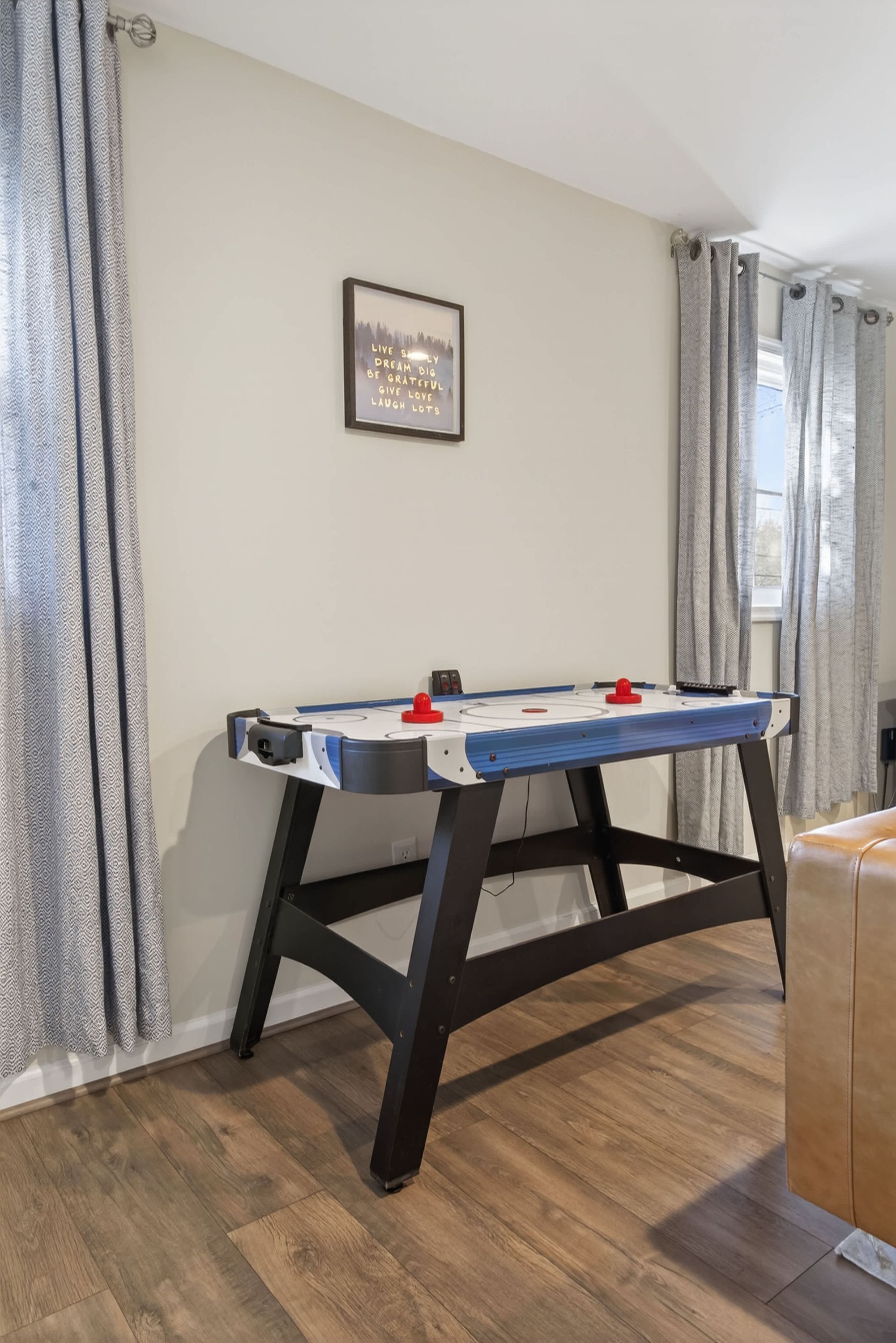 Una habitación con mesa de fútbol de mesa, una cita inspiradora enmarcada en la pared y una ventana con cortinas.