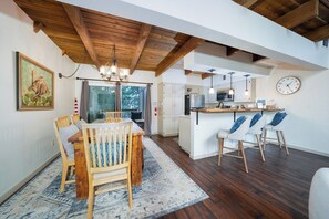A dining area with a wooden table and chairs, a kitchen with white cabinets, and a clock on the wall. - Innsbrook Vacation Townhome 23 (Ruidoso)