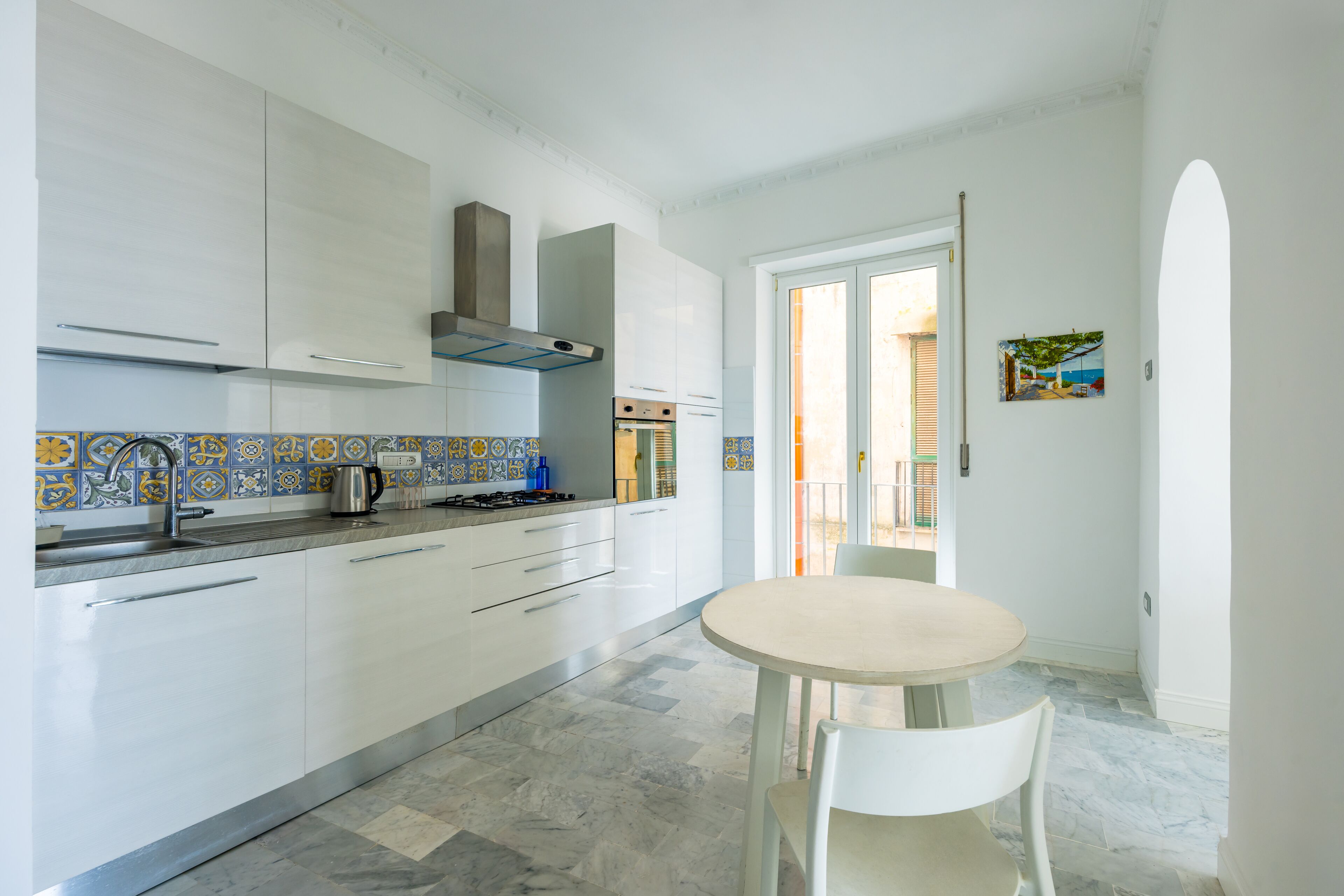 A modern kitchen with white cabinets, a tiled backsplash, a gas stove, and a round table with a chair.