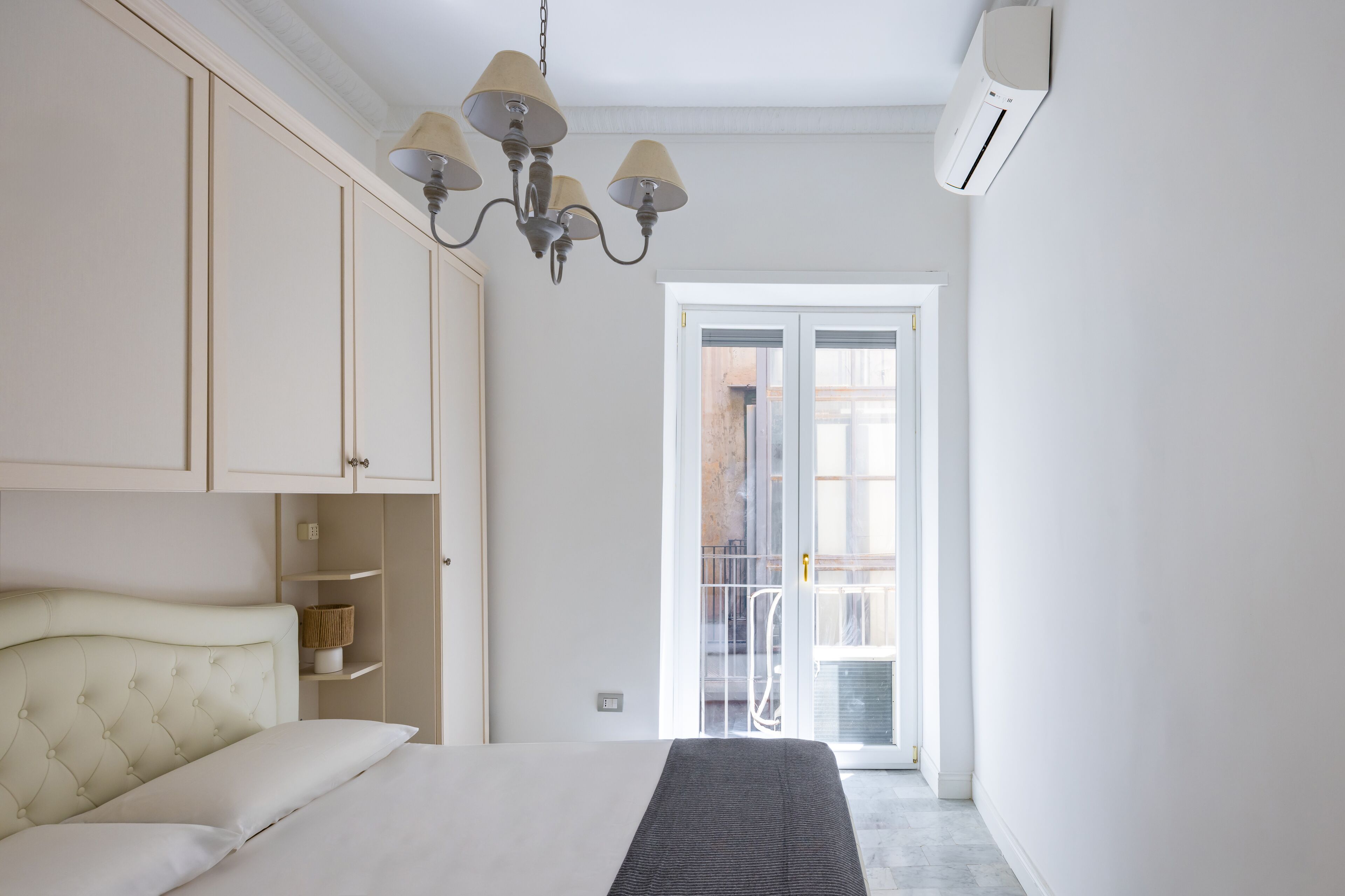 A bedroom with a bed, a wardrobe, a chandelier, and a sliding glass door leading to a balcony.