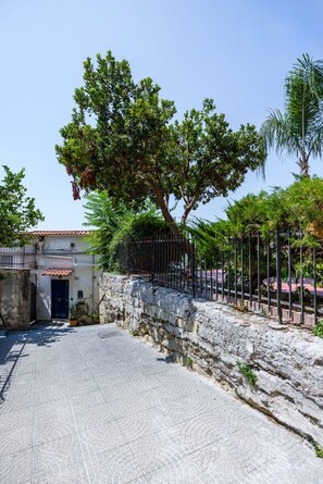 Pátio pavimentado com muro de pedra, cerca de metal e um edifício com telhado de telhas.