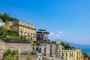 Eine Küstenstadt mit historischen, gelben Gebäuden, einer Steinbefestigung und Blick auf das Meer und ein Bergmassiv.