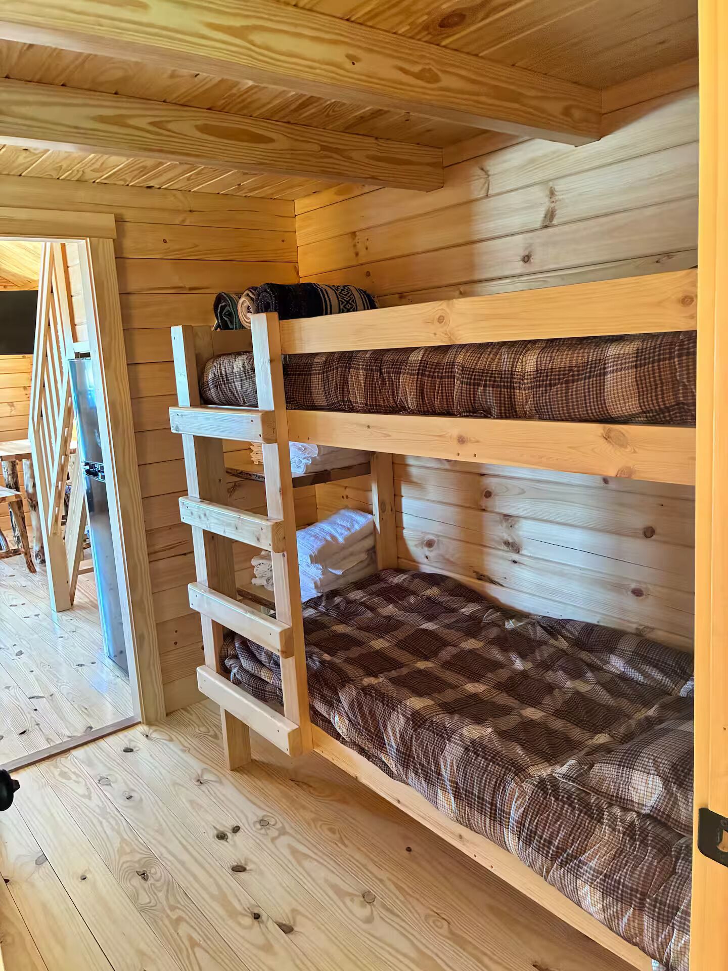 A wooden bunk bed with a ladder, checkered bedding, and a wooden floor.
