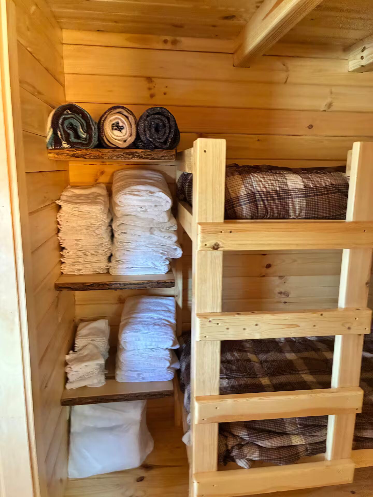 A wooden storage unit with shelves holding folded towels and a wooden ladder.