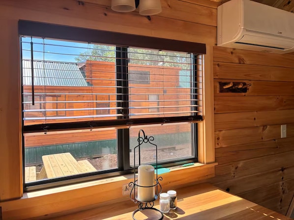 A room with a large window, wooden walls, a small table with a candle holder, and a visible air conditioning unit.