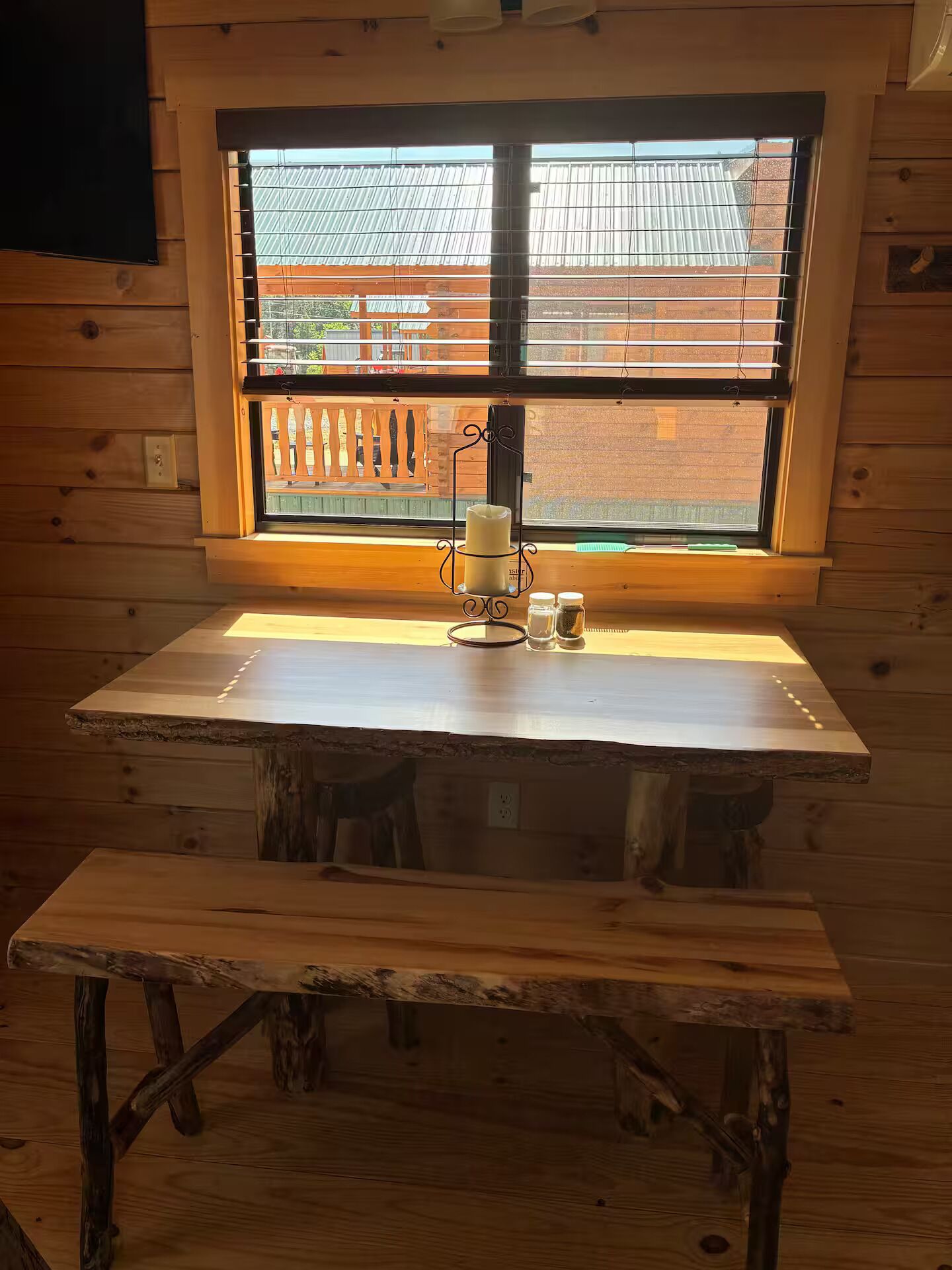 Un tavolo di legno con una candela e salsiere vicino a una finestra con persiane.