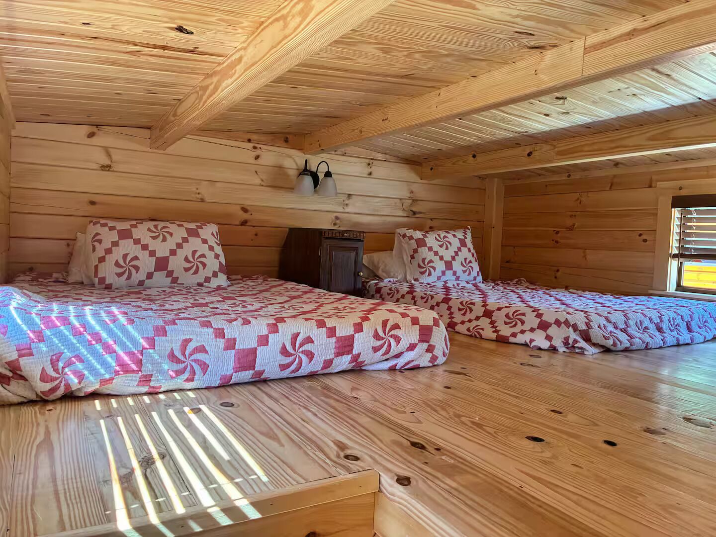 Una cabaña con dos camas de madera, un mueble pequeño y una ventana con persianas.