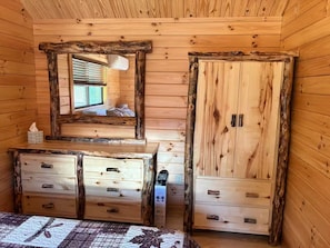 A wooden cabin room with a bed, dresser, mirror, and wardrobe.