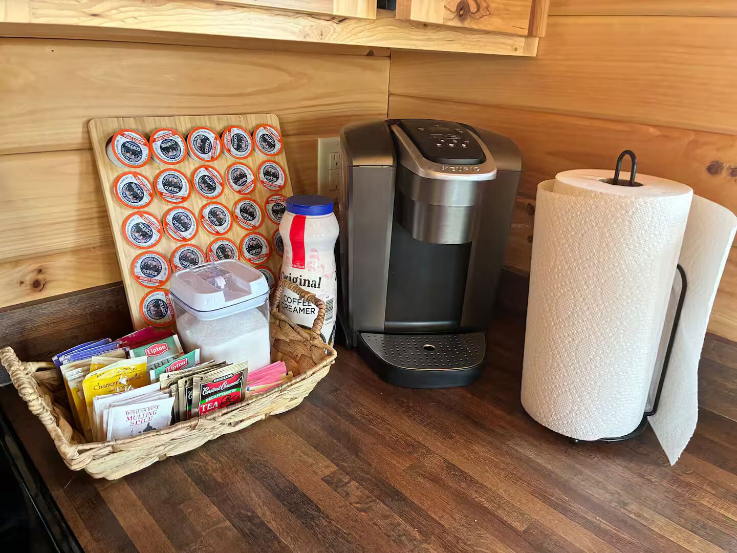 A kitchen with a coffee maker, a basket of tea bags, and a stack of paper towels.