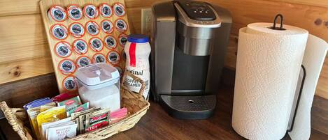 A kitchen with a coffee maker, a basket of tea bags, and a stack of paper towels.