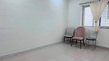 Una habitación con suelo de baldosas, una ventana con cortinas y dos sillas.