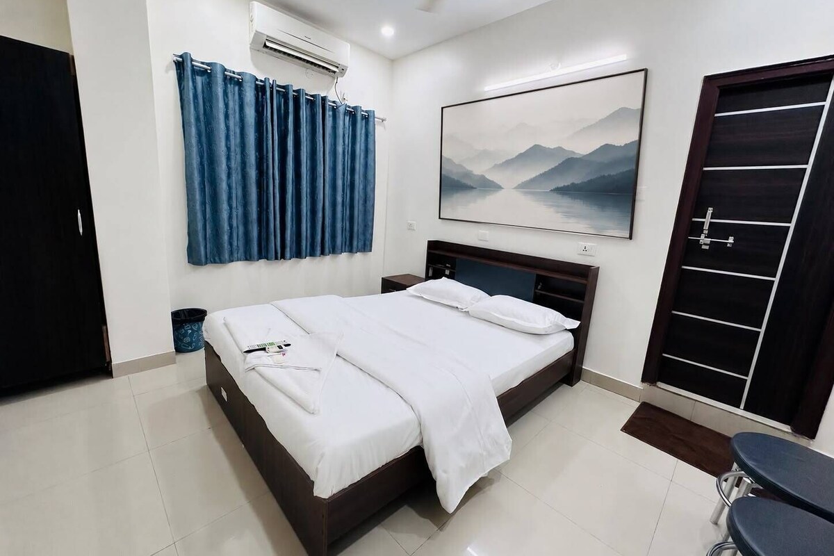 Een hotelkamer met een bed, nachtkastje, bureau, stoel, deur en een wandairconditioner.