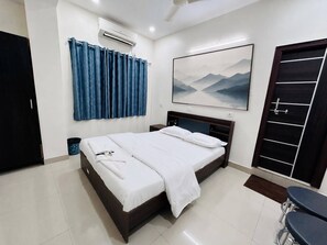 Een hotelkamer met een bed, nachtkastje, bureau, stoel, deur en een wandairconditioner.