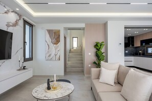 Ein modernes Wohnzimmer mit einem Marmortisch, einem beigefarbenen Sofa und einem großen, an der Wand befestigten Flachbildfernseher.