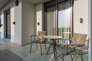 Ein Balkon mit zwei Stühlen, einem kleinen runden Tisch, einer Schiebeglastür und einer wandmontierten Leuchte.