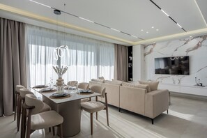 Ein modernes Wohnzimmer mit Essbereich, ausgestattet mit einer Sofagarnitur, einem Esstisch mit Stühlen und einem an der Wand montierten Flachbildfernseher.