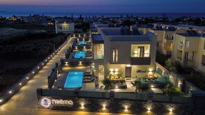 A modern resort with multiple swimming pools, a well-lit pathway, and a view of the sea. - Noema Luxury Villas - Villa Nemesis, by Estia (Kato Gouves)