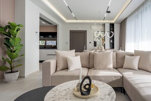 A modern living room with a sectional sofa, a marble coffee table, and a large potted plant. - Noema Luxury Villas - Villa Iris, by Estia (Kato Gouves)