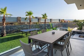 An outdoor patio with a ping pong table, seating, and a view of the sea. - Noema Luxury Villas - Villa Iris, by Estia (Kato Gouves)