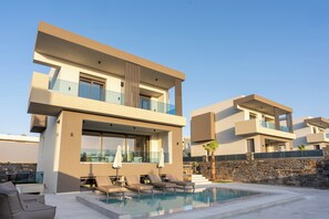 Un edificio residenziale moderno su due piani con piscina, area salotto esterna e un muro in pietra.