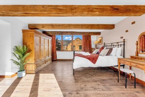 A bedroom with a large bed, wooden wardrobe, and a view of a building through a window. - Oxhay Barn (Newcastle-Under-Lyme)