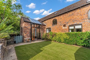 A brick house with a glass conservatory, a well-maintained lawn, and a hedge. - Oxhay Barn (Newcastle-Under-Lyme)