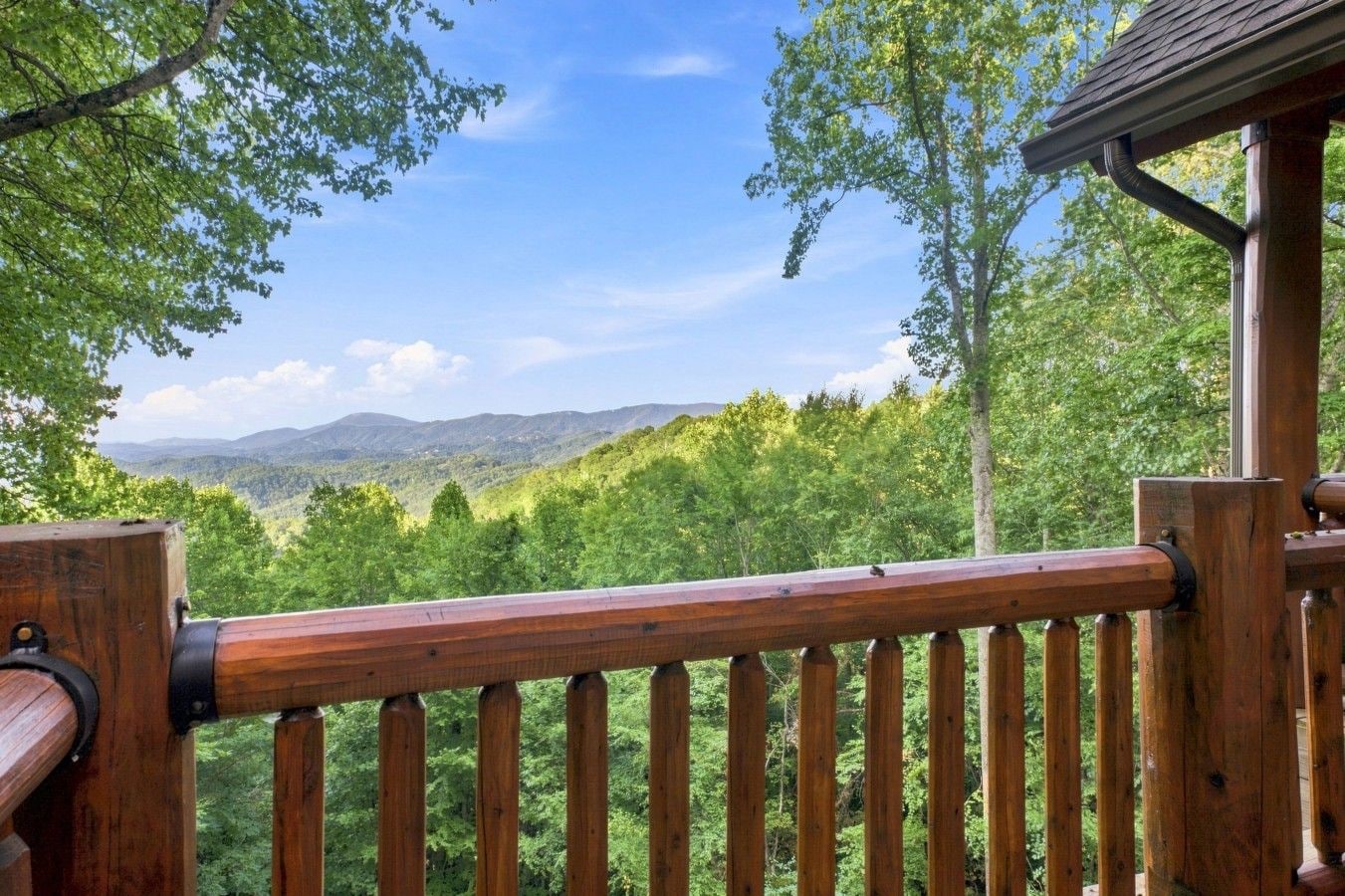 A wooden deck railing overlooking a forested landscape with distant mountains.