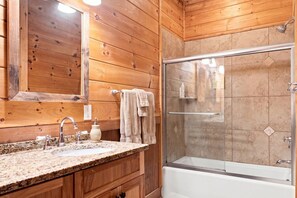 Bagno di una baita in legno con lavabo su piano in granito, box doccia in vetro e pareti in legno.