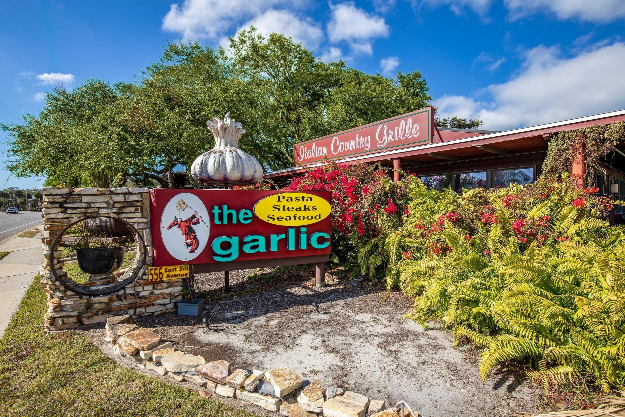 Une enseigne de restaurant pour « The Garlic », avec un logo, une liste de plats et l’adresse.