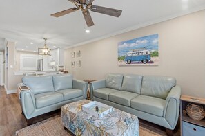 A living room with a ceiling fan, a painting of a van, and a sofa. - Sea Coast Gardens III 216 (New Smyrna Beach)