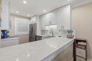 A modern kitchen with white cabinetry, stainless steel appliances, and a marble countertop. - Sea Coast Gardens III 216 (New Smyrna Beach)